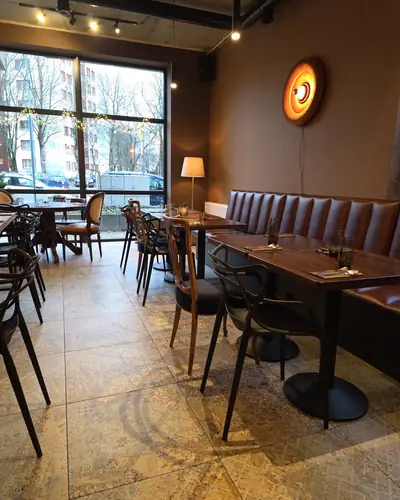 Sala restauracji z drewnianymi stołami, kanapą i dużymi oknami
